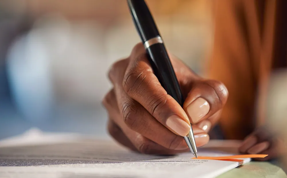 Close-up of a hand writing notes at a desk